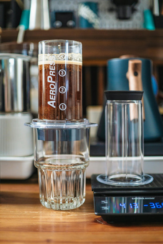 AeroPress coffee brewer sitting atop a glass on a counter.  A scale is adjacent to the brewer.